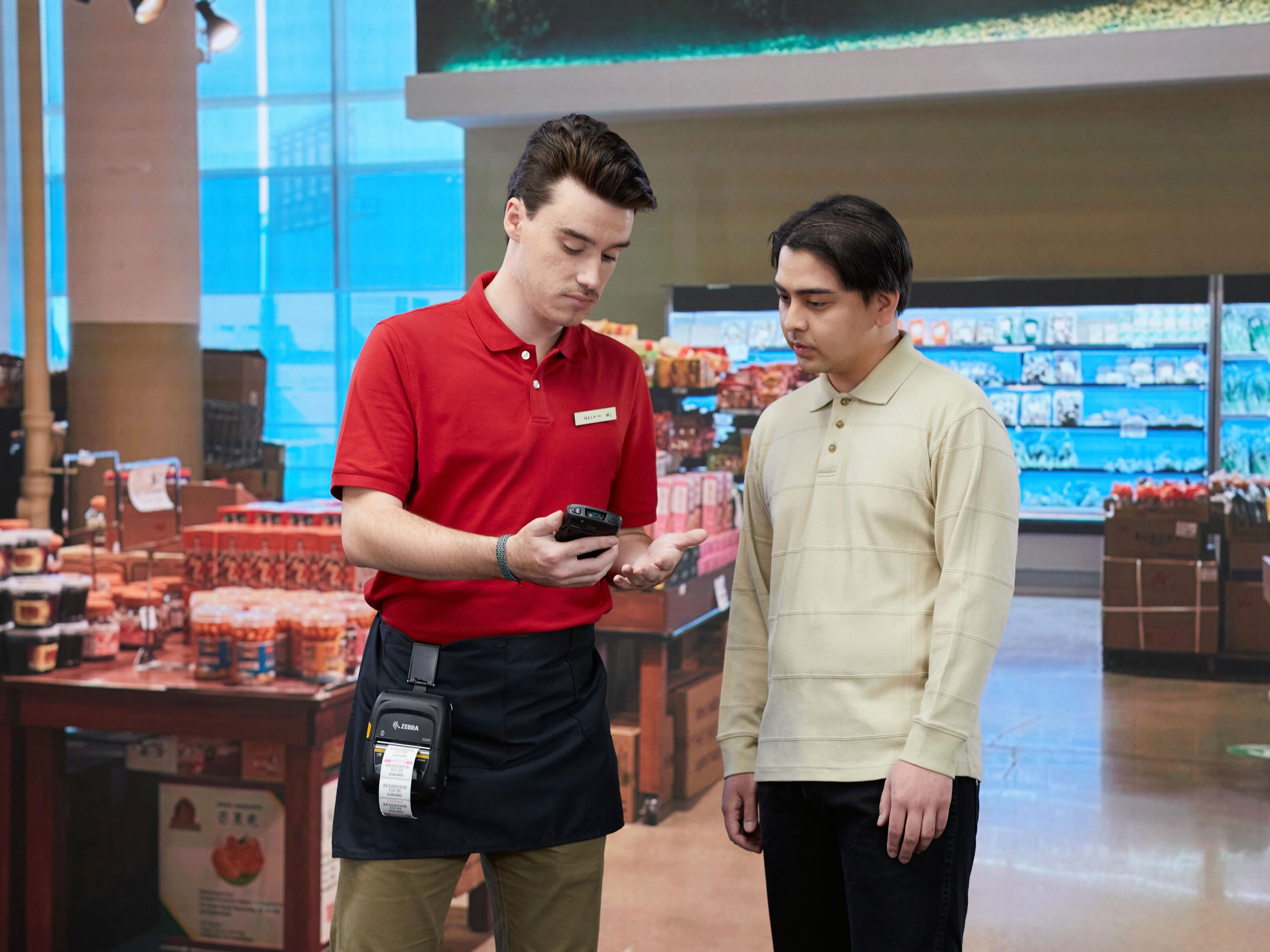 A retail associate looks at his Zebra mobile device while helping a shopper