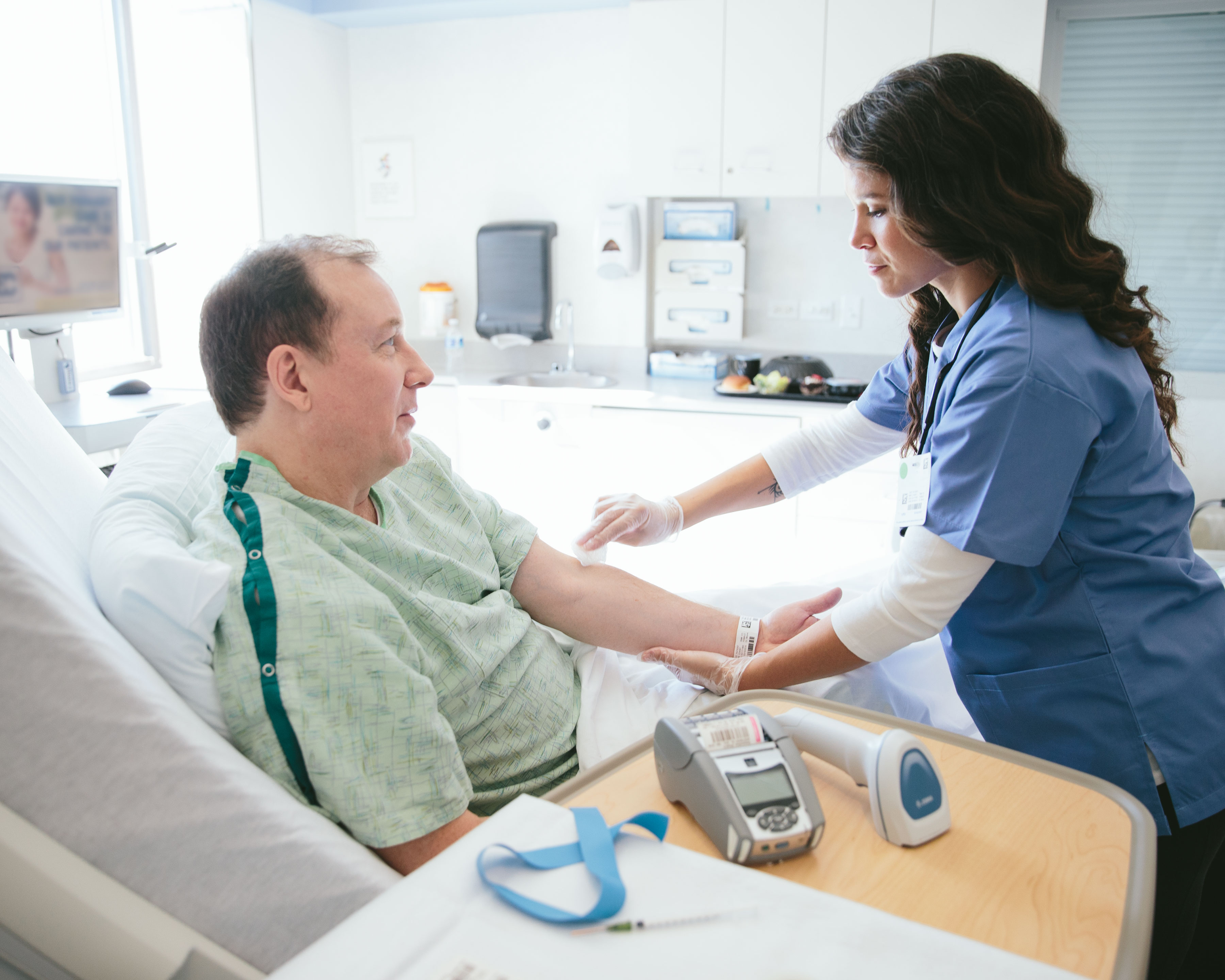 Zebra DS8100 handheld barcode scanner placed on an overbed table as healthcare worker prepares to draw blood of a patient