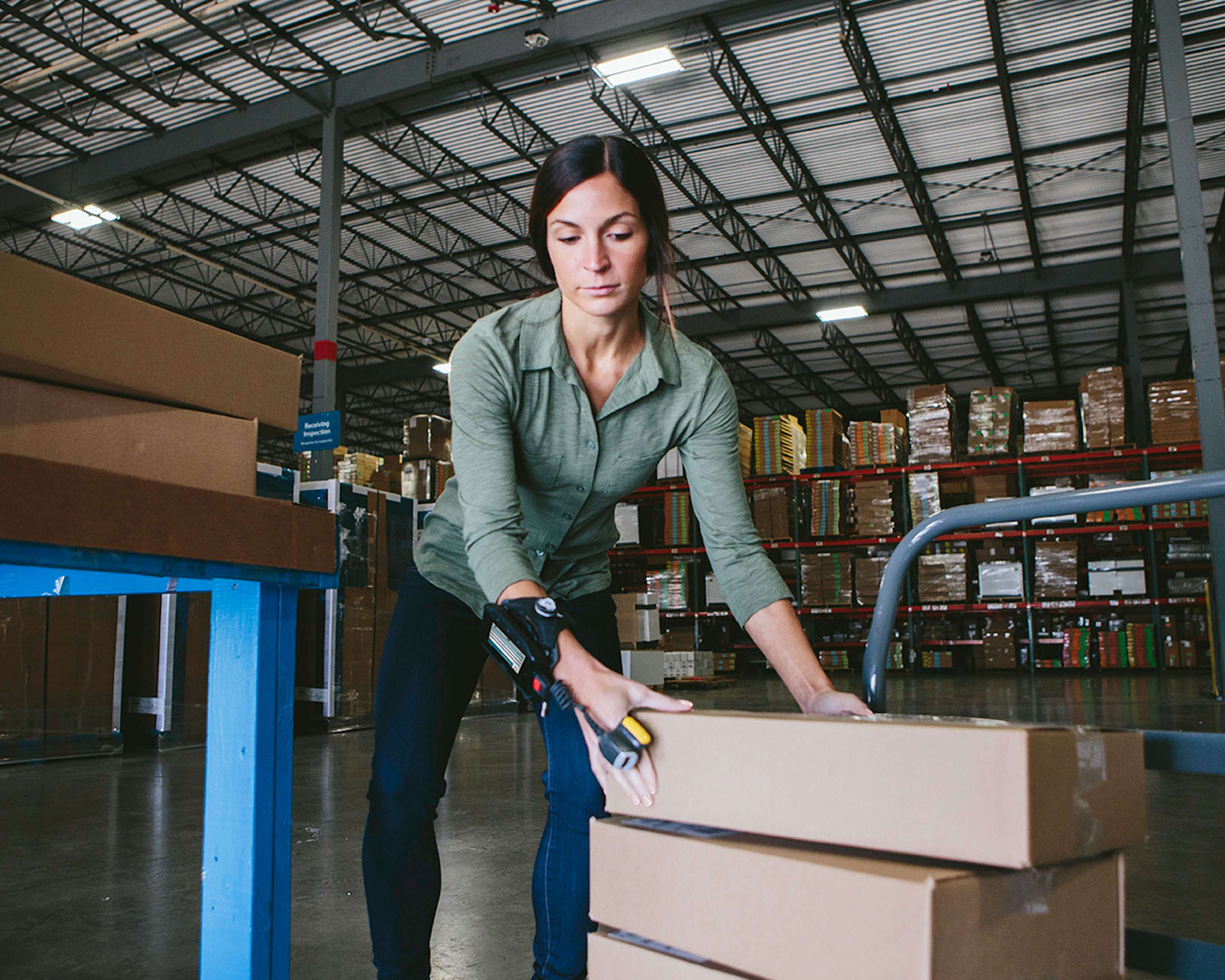 Warehouse worker wears Zebra RS5000 ring scanner as she loads shipping boxes on a push cart dolly