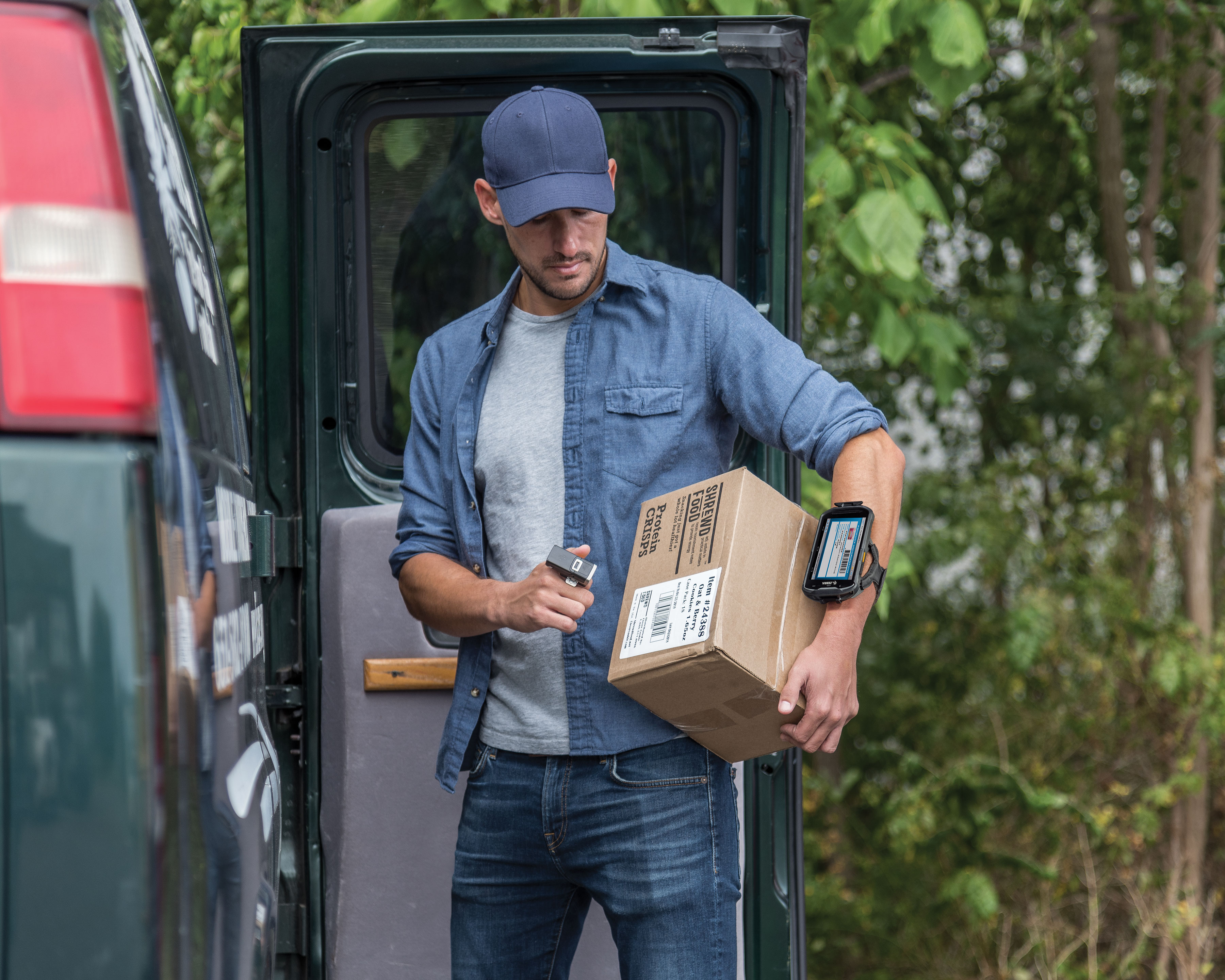 Zebra TC5x mobile computer shows package information as the worker scans the brown box uses the Zebra RS5100 wireless Bluetooth barcode scanner on his left index finger