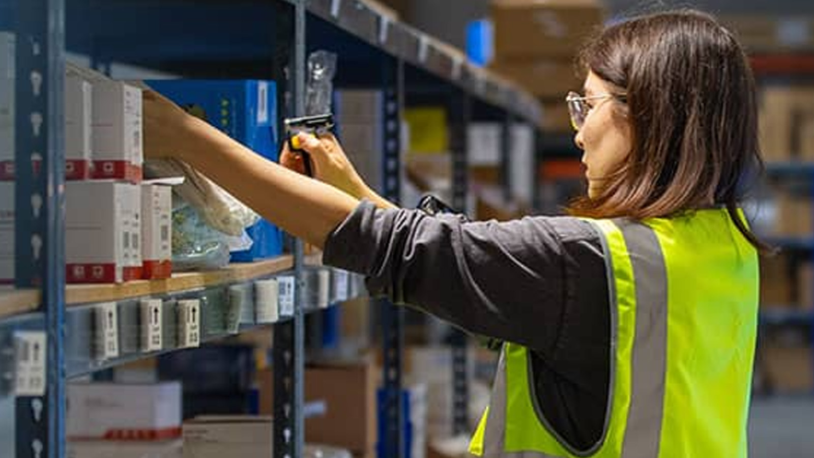 A worker in a high-visibility vest scans an item on a warehouse shelf, effectively utilizing the Team Intelligence system to coordinate seamlessly with autonomous mobile robots and boost efficiency.