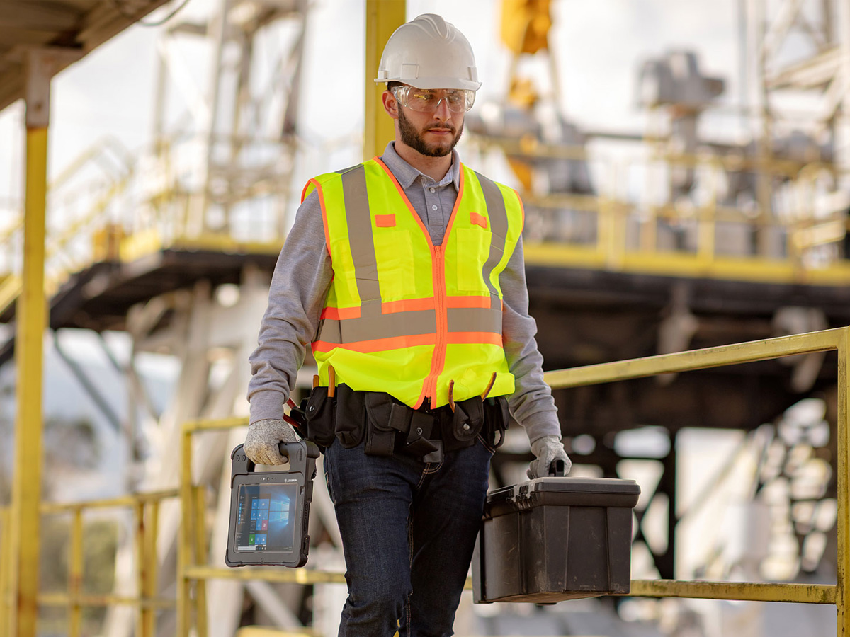 Utilities worker holding a zebra tablet walking on catwalk