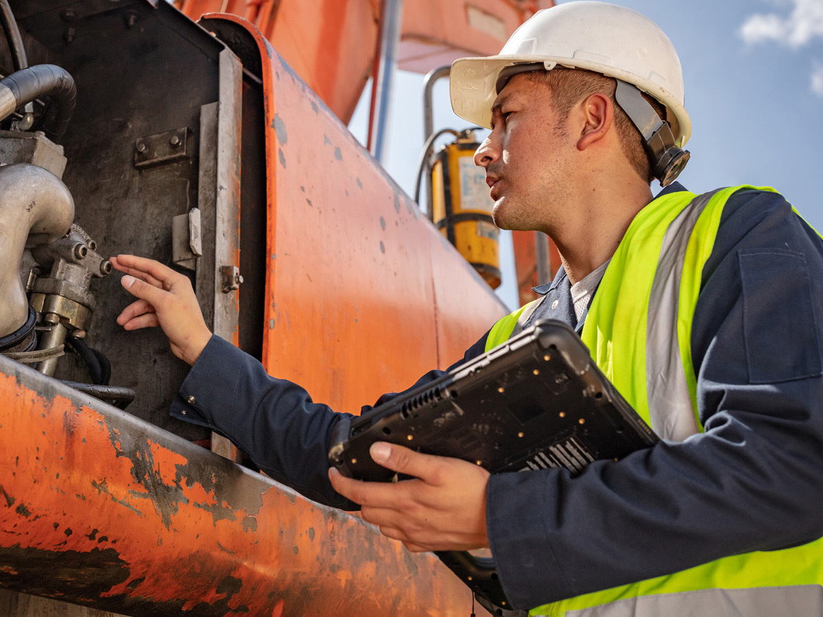 Worker with white hard hat inspecting pipes while holding a zebra tablet