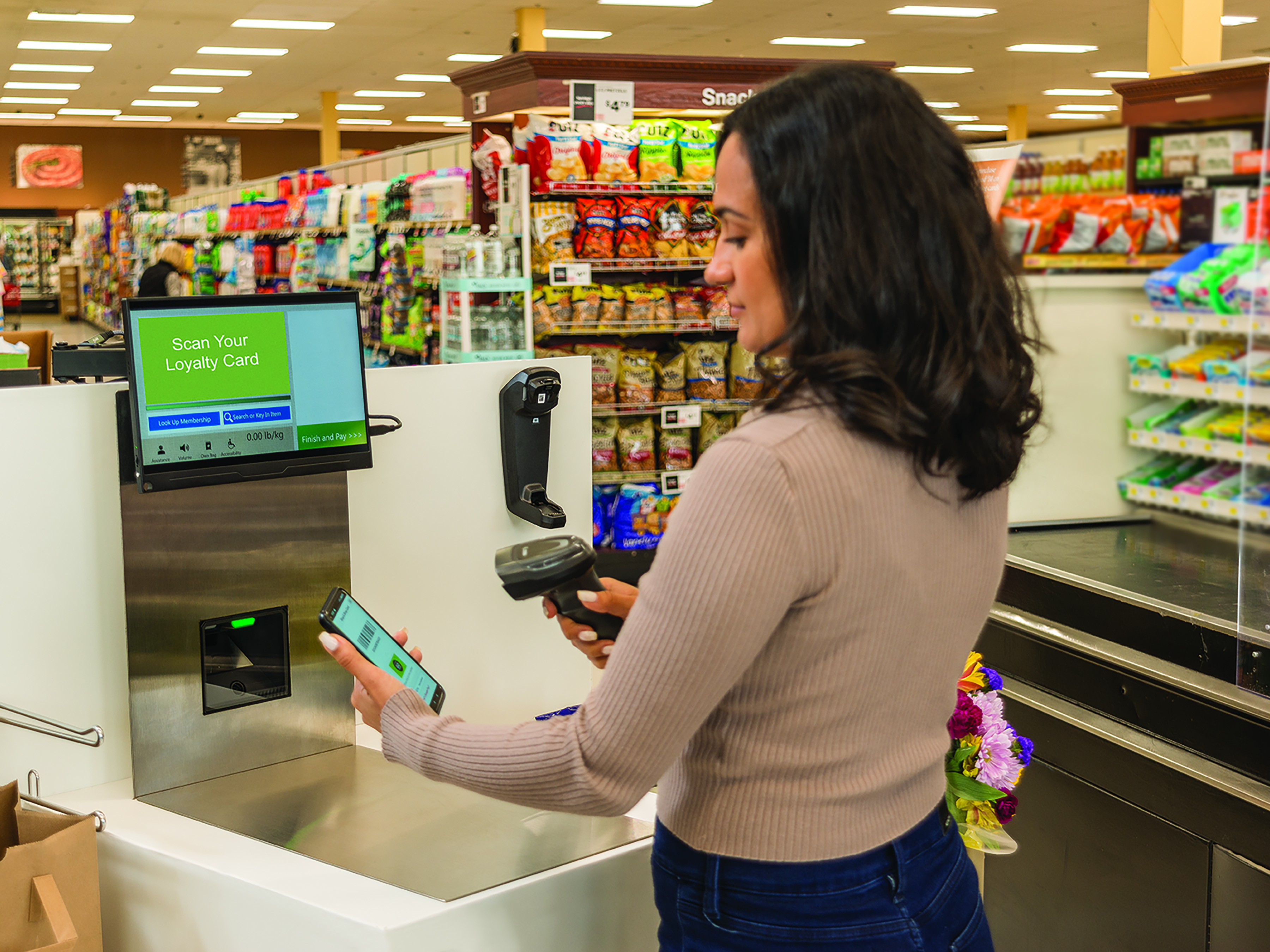 A woman uses a cordless Zebra barcode scanner to scan a QR code in her mobile app at the self-checkout lane  