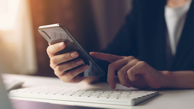 Persona frente a un teclado sosteniendo y mirando su teléfono inteligente